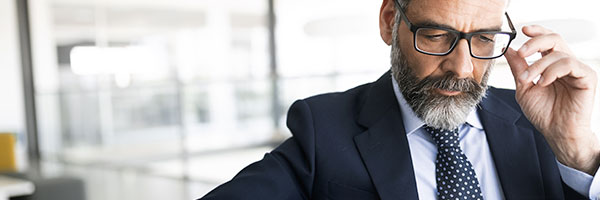 Cuentas Banca Privada - Asesor financiero con traje, corbata y gafas mirando una tablet sentado en una silla en la oficina Cuentas Banca Privada - Asesor financiero con traje, corbata y gafas mirando una tablet sentado en una silla en la oficina
