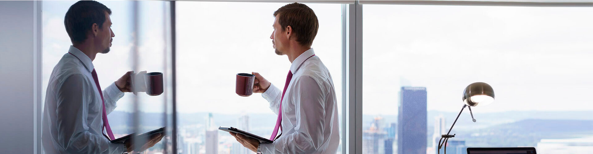 Factoring Internacional - Un hombre con camisa y corbata, con una taza en la mano mirando por la ventana