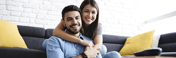 Seguro de Accidentes RGAPersonalPlus - Pareja joven sonriendo en el salón de su casa con portátil