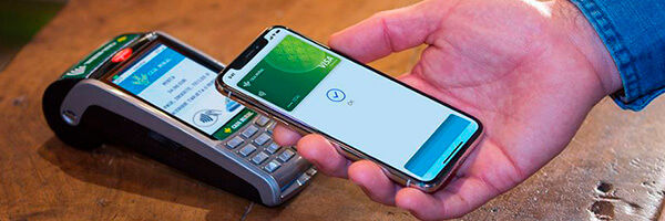 Apple Pay - Persona pagando con apple pay en su movil en el tpv de un comercio Apple Pay - Persona pagando con apple pay en su movil en el tpv de un comercio