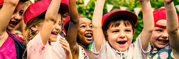 Promociones y concursos de Programa En Marcha - Niños con las manos levantadas sonriendo en un campamento de verano Promociones y concursos de Programa En Marcha - Niños con las manos levantadas sonriendo en un campamento de verano