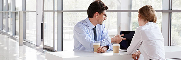 Financiación internacional - Reunión de negocios entre un hombre y una mujer de negocios con camisa, frente a un portátil hablando y tomando café Financiación internacional - Reunión de negocios entre un hombre y una mujer de negocios con camisa, frente a un portátil hablando y tomando café