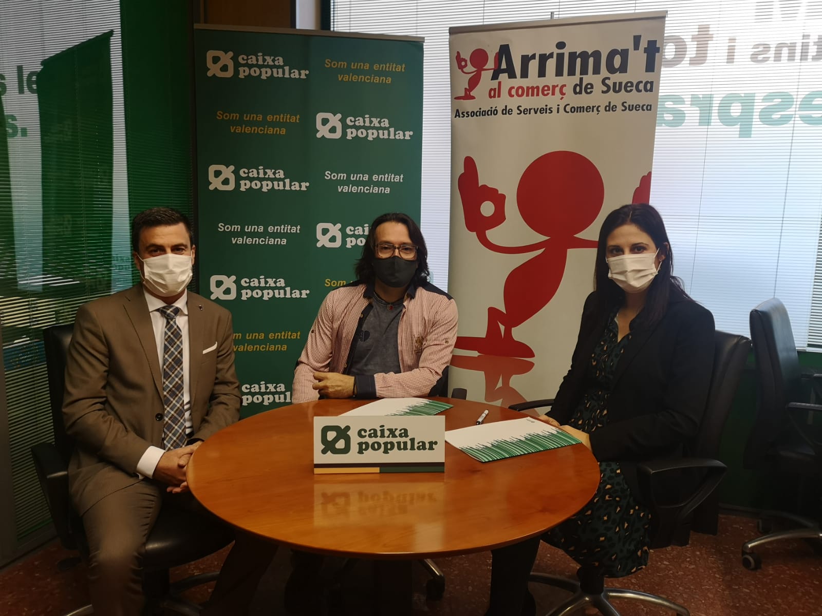 Representantes de Caixa Popular y de la Asociacion de comerciantes de Sueca sentados a una mesa firmando el convenio Representantes de Caixa Popular y de la Asociacion de comerciantes de Sueca sentados a una mesa firmando el convenio