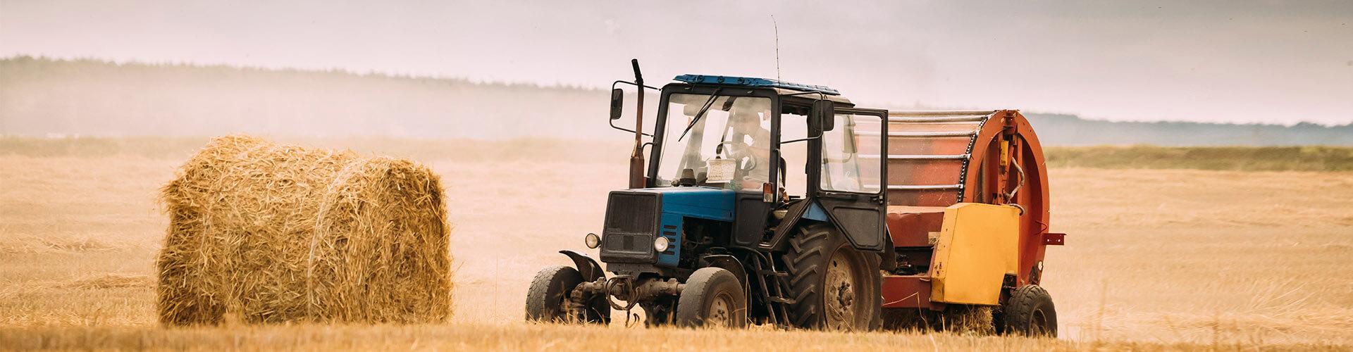 Assegurances Agràries - Tractor blau en el camp recollint palla per a donar menjar al bestiar