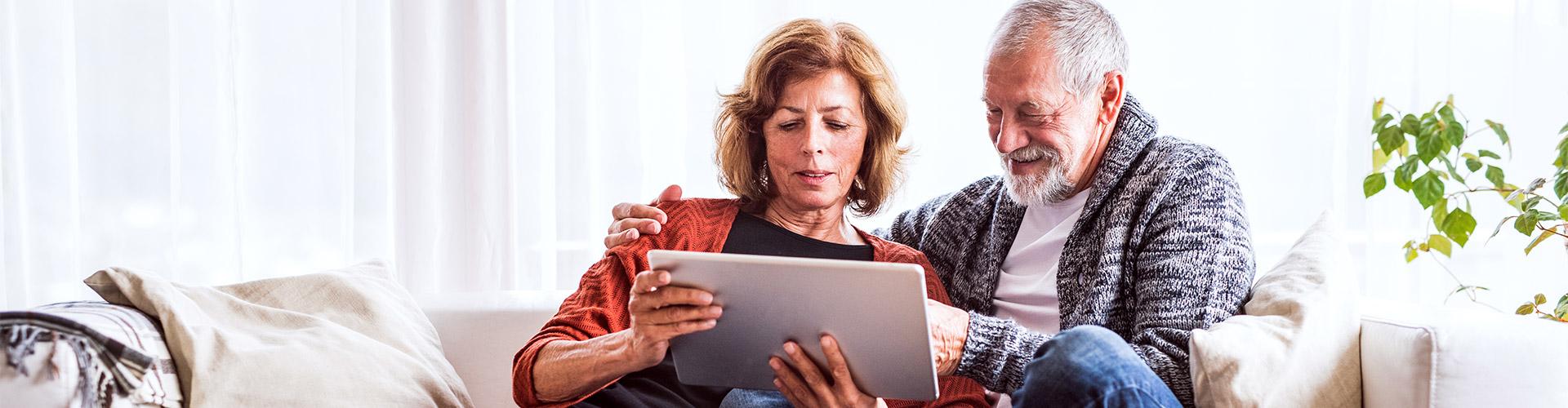 Cliente Pensión - Una pareja jubilada relajada en casa utilizando una tableta digital
