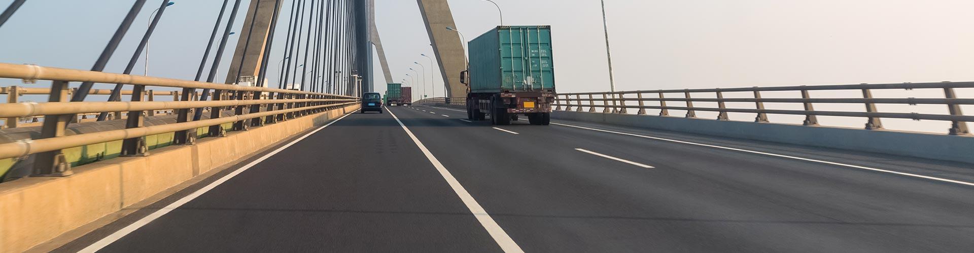 Segur de Transports - Carretera d'una ciutat on circulen camions de transport de mercancias al costat d'un pont