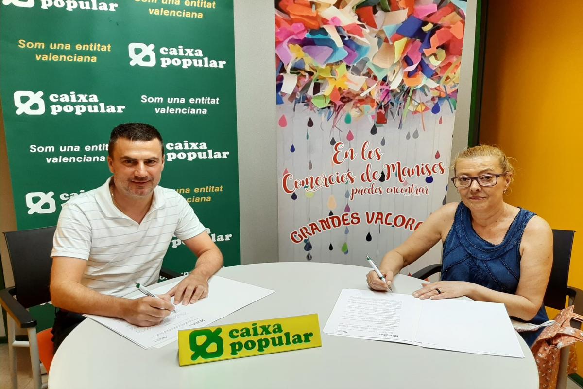 La presidenta de ASCOMA i el Director de l'Oficina de Caixa Popular de Manises asseguts signant conveni