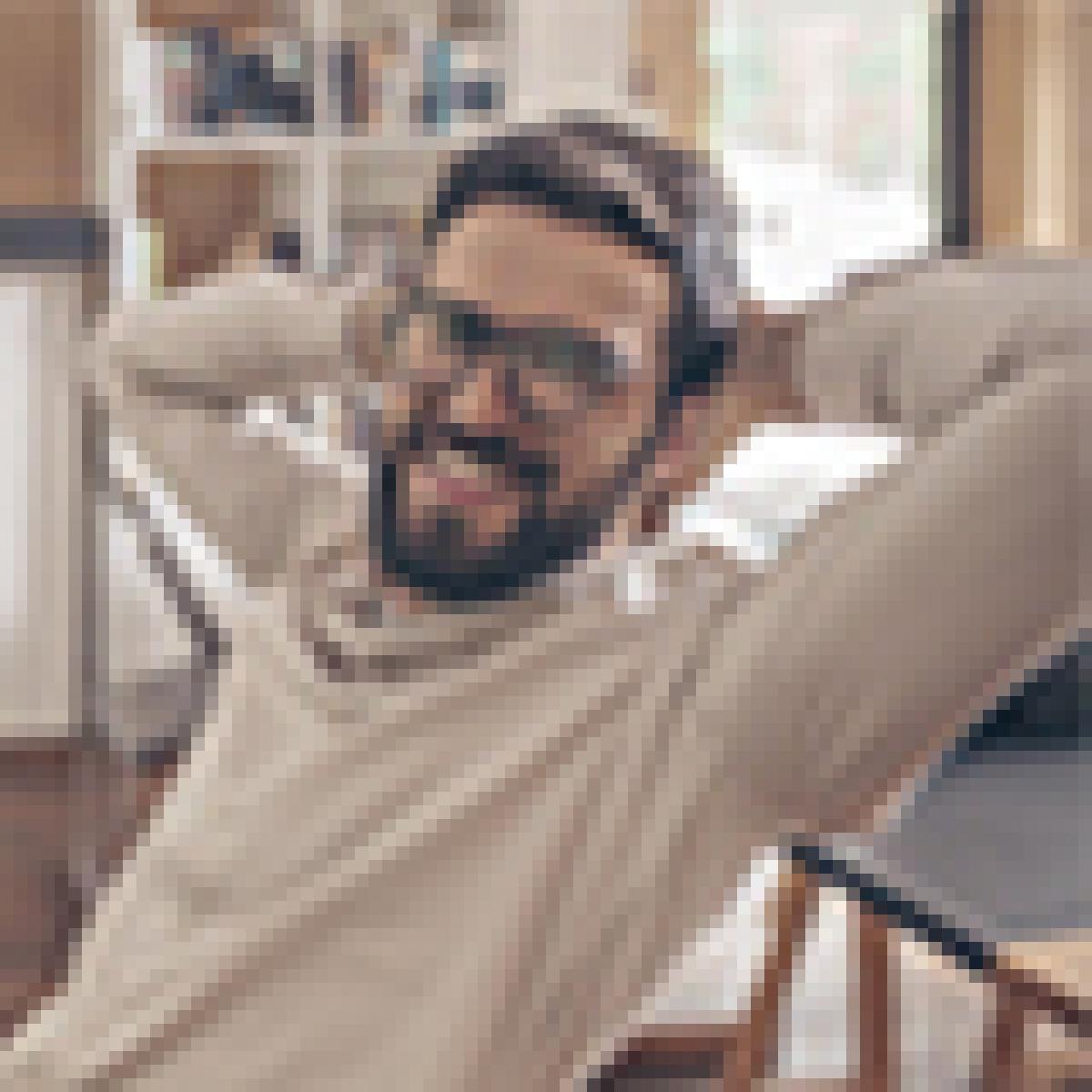 El meu primer treball - Xic jove amb ulleres somrient assegut en una cadira a la biblioteca mentre estudia