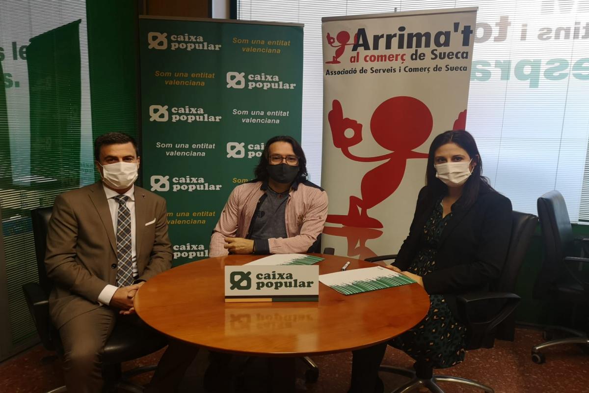 Representantes de Caixa Popular y de la Asociacion de comerciantes de Sueca sentados a una mesa firmando el convenio