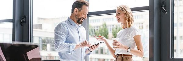 Cartera Premium - Hombre con camisa y movil en la mano, y mujer de negocios con cafe en la mano sonriendo en la oficina