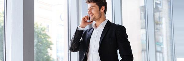 Prestamos en Divisas - Hombre de negocios con camisa blanca y traje negro sonriendo, andando por la calle y hablando por el movil Prestamos en Divisas - Hombre de negocios con camisa blanca y traje negro sonriendo, andando por la calle y hablando por el movil
