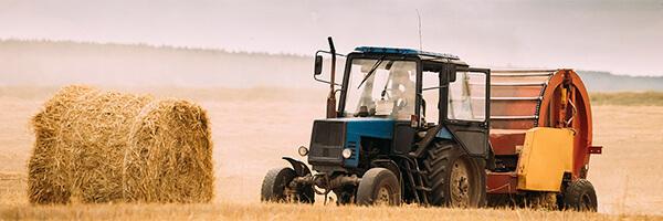 Assegurances Agràries - Tractor blau en el camp recollint palla per a donar menjar al bestiar