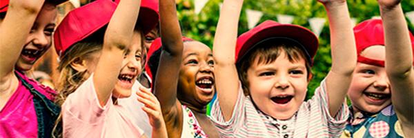 Promociones y concursos de Programa En Marcha - Niños con las manos levantadas sonriendo en un campamento de verano