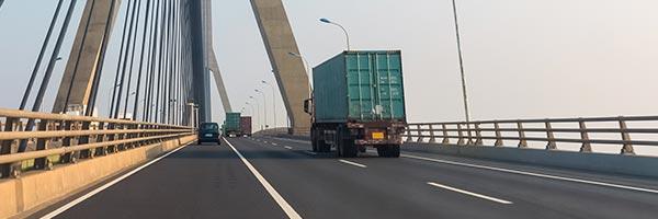 Segur de Transports - Carretera d'una ciutat on circulen camions de transport de mercancias al costat d'un pont