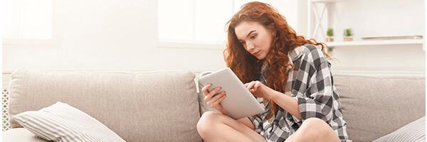 Compte de Pagament Bàsic - Chica jove amb una camisa de quadres asseguda en el sofà de la seua casa amb una tablet
