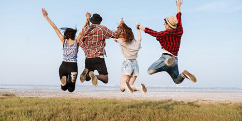 Promoció Canviar compte - Joves feliços i somrient saltant en l'aire enfront de la platja
