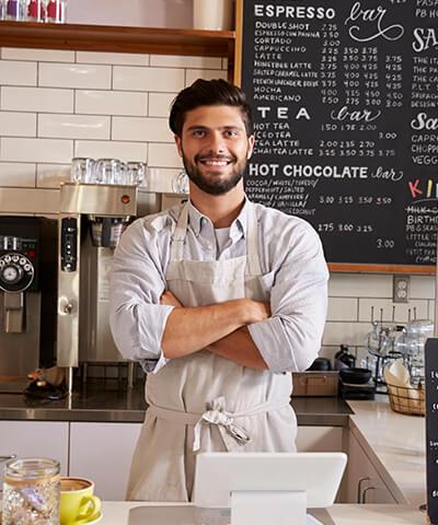Avantatges per a Autònoms - L'amo d'una cafeteria amb els braços creuats somrient darrere de la barra del seu negoci